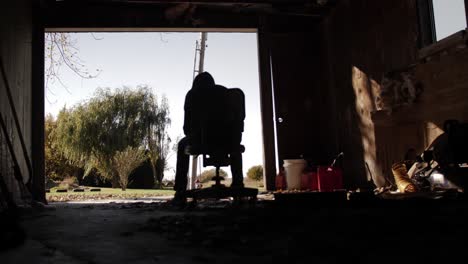 handheld shot of silhouette of lonely, sad teenage boy sitting in a dark and dirty garage