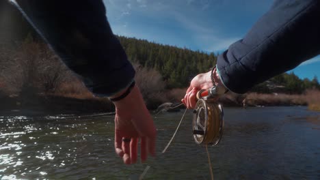 POV-hands-using-fly-fishing-rod,-reeling-in-golden-line-at-trout-river