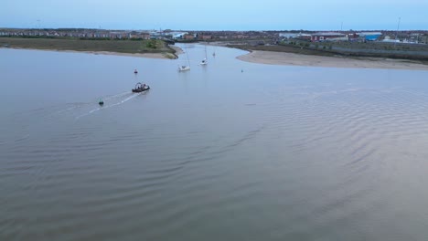 Pilot-boats-following-yachts-into-marina-entrance-on-calm-water-at-dusk-on-the-River-Wyre-Estuary-Fleetwood-Lancashire-UK