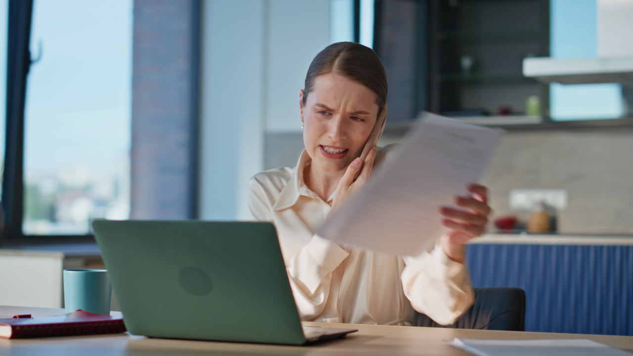 Dissatisfied woman talking mobile phone reviewing documents at workplace closeup