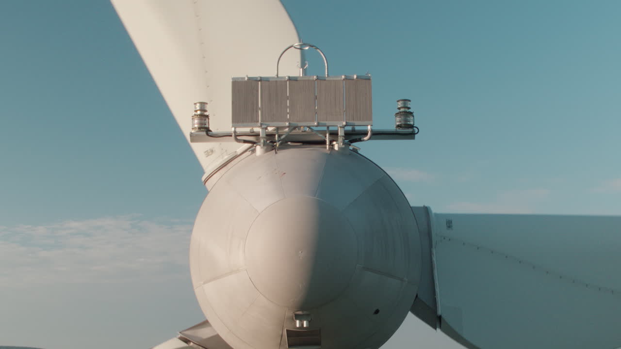 As the drone hovers behind, a towering wind turbine enters the frame in warm sunset light. Behind it, turbines stretch across glowing hills—perfect for cinematic energy or sustainability projects.