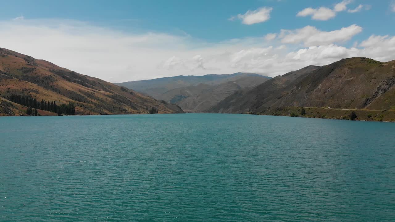 cámara lenta - antena - represa clyde, lago dunstan, otago central, nueva zelanda con montañas y nubes en el fondo