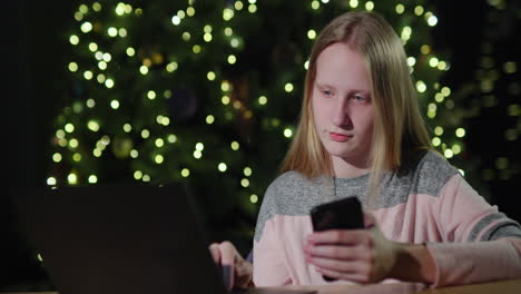 a teenage girl uses a smartphone on the background of a christmas tree