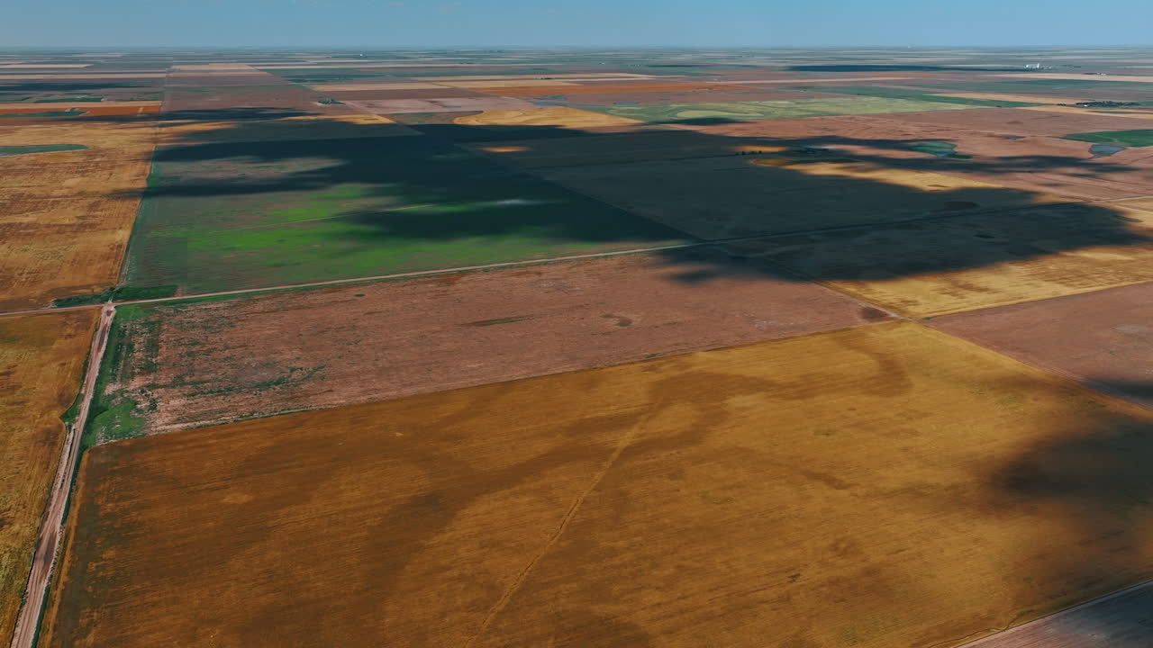 Huge field looking like a patchwork quilt. A shadow of a big cloud is on the ground. Top view.