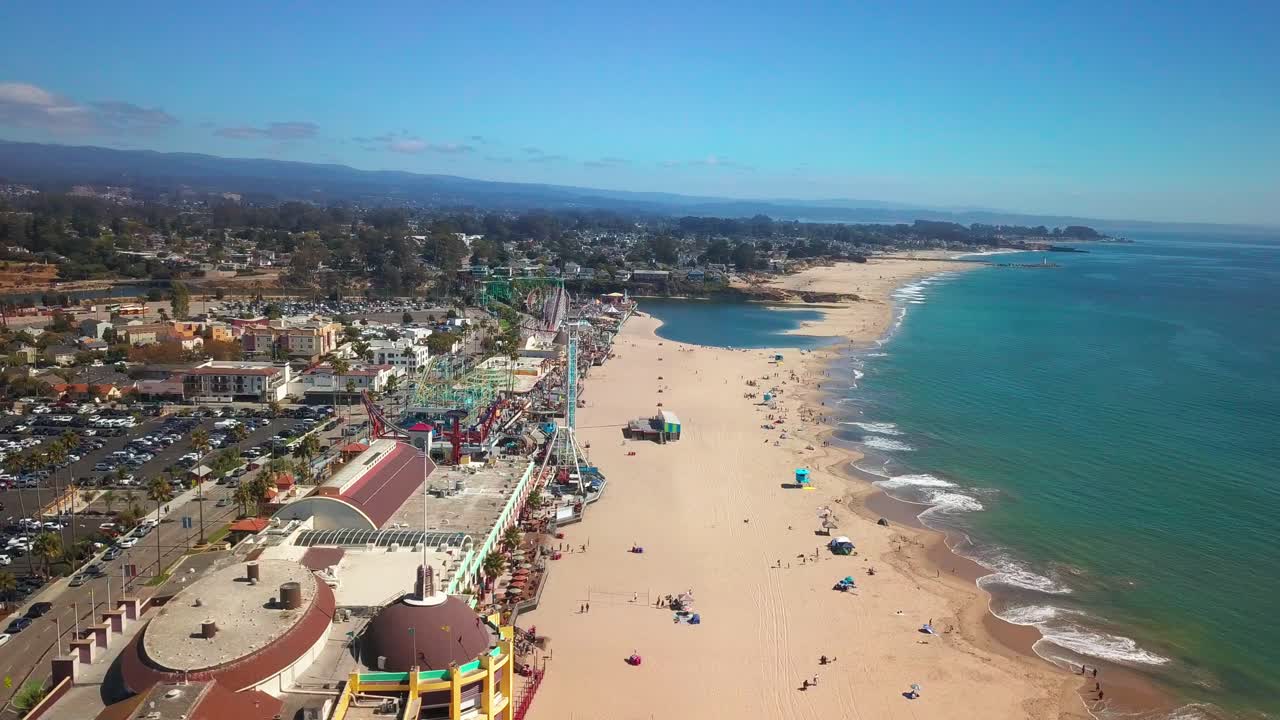 Aerial dolly across ocean and beach to boardwalk amusement park. 4K