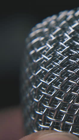 mature person holds modern shining metallic microphone on dark background extreme close view