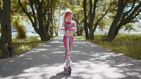 Young-athletic-fit-blonde-girl-rides-traveling-on-electric-scooter-on-road-in-park-on-sunny-day