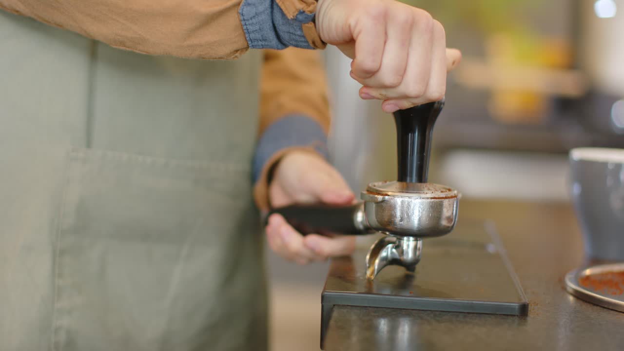Barista concentrata con il portafiltro, in grembiule che pressa il caffè sul bancone per preparare l'espresso