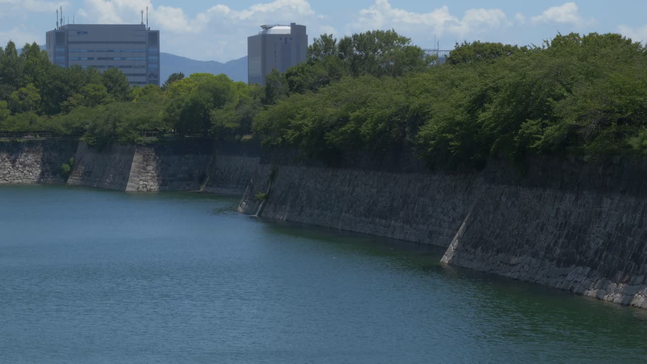 Green Trees Over The Stone Walls Of Moat At Osaka Castle Park In Japan. - wide shot