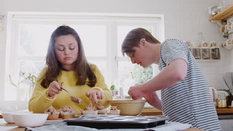 Pareja-Joven-Con-Síndrome-De-Down-Decorando-Pastelitos-Caseros-Con-Glaseado-En-La-Cocina-De-Casa