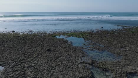 Low-angle-drone-shot-of-low-tide-reef-and-waves-in-Uluwatu-Bali-Indonesia