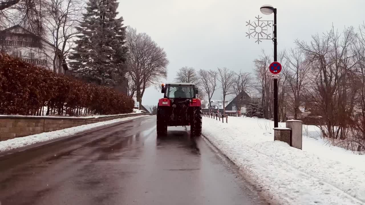 el tractor conduce a través del pueblo de invierno con nieve ligera pasando por casas pequeñas