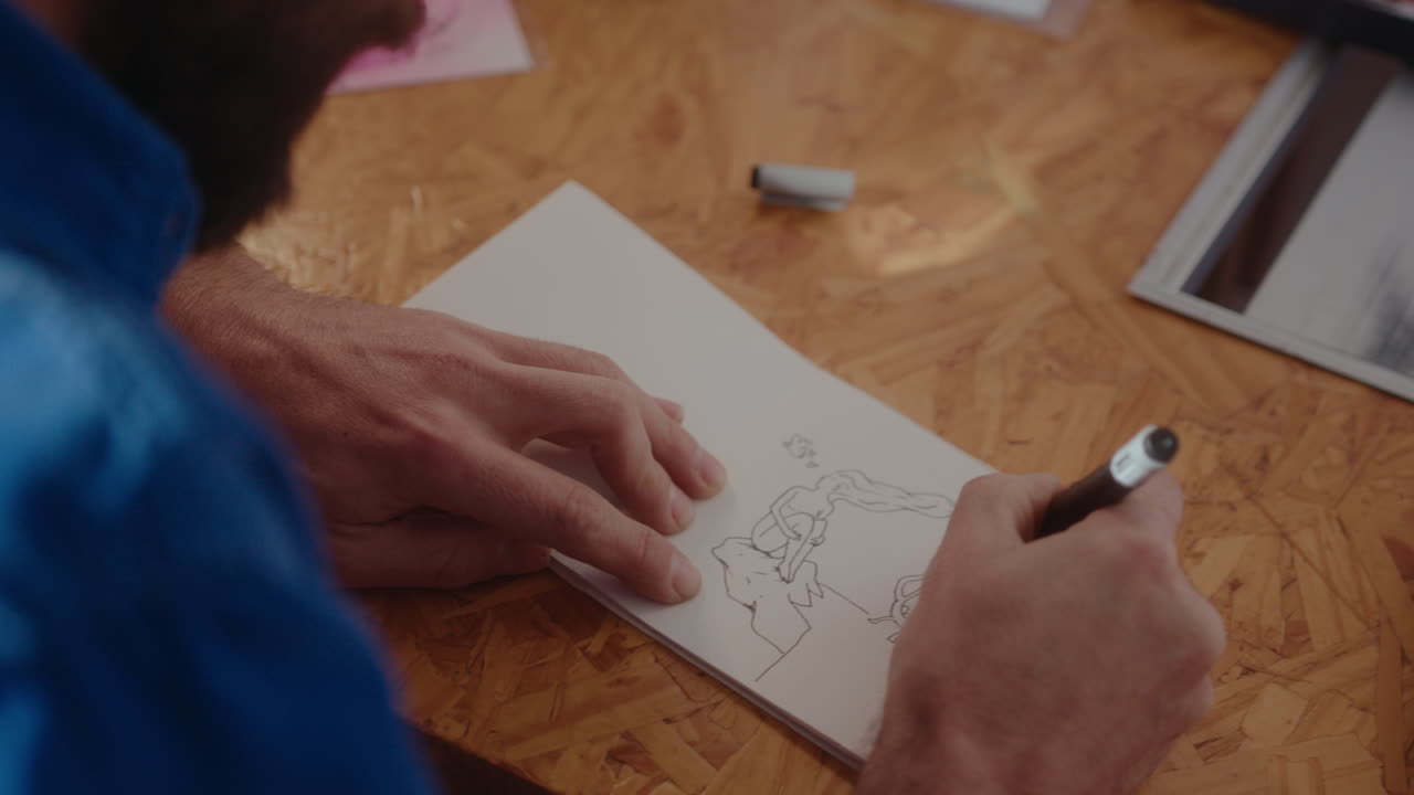 Artist Drawing Picture in a Sketchbook at Desk
