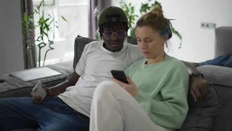 pareja biracial relajándose feliz en el sofá con un teléfono inteligente