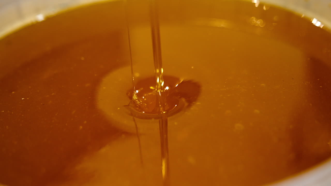 Golden liquid freshly gathered honey in a bowl. Little streams filling the dish. Healthy organic natural food concept close up.