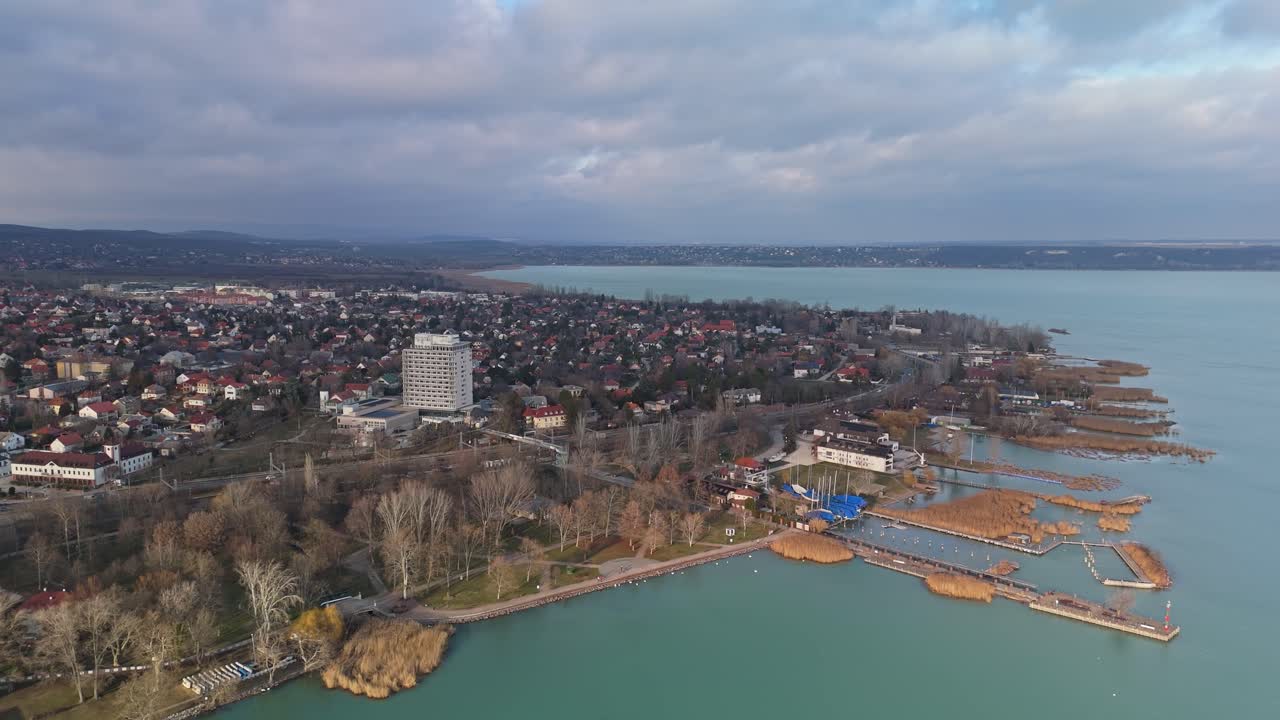Macaristan, Balatonalmádi'nin kuşbakışı görüntüsü, Balaton Gölü kıyısı boyunca marinasını, sahil şeridini ve kentsel manzarasını tekneler, oteller, yapraklarını dökmüş ağaçlar ve arka planda bulutlu bir kış gökyüzüyle sergiliyor.
