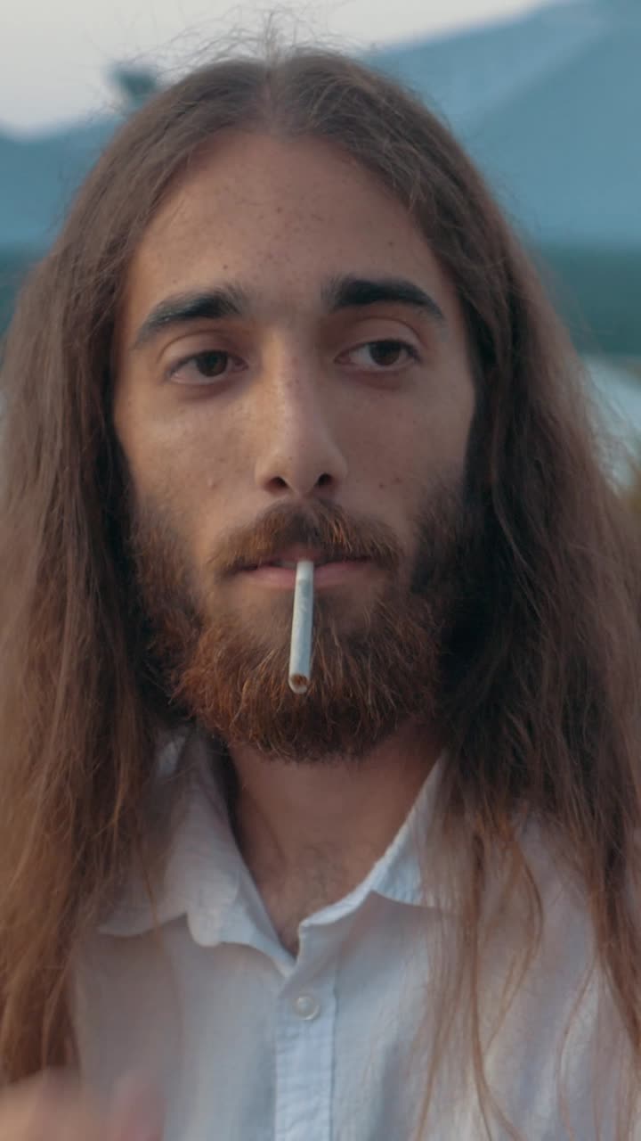Primer plano de un joven con pelo largo encendiendo un cigarrillo