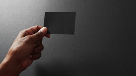 mano de un hombre biracial con una tarjeta de visita negra en un fondo gris, espacio de copia, cámara lenta