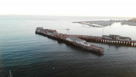 aerial drone shot over stearns wharf pier and sailboats in the blue ocean near santa barbara harbor, california