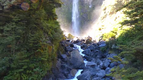 upwards tilt through water spray of incredible waterfall in early-morning sunshine - devil's punchbowl waterfall walk, arthur's pass national park