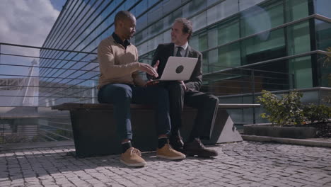 multiethnic colleagues with laptop shaking hands outdoors