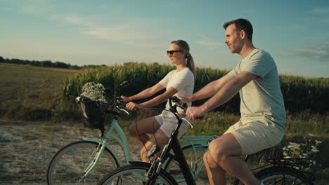 side view of playful caucasian couple having fun while riding a bike on village road.