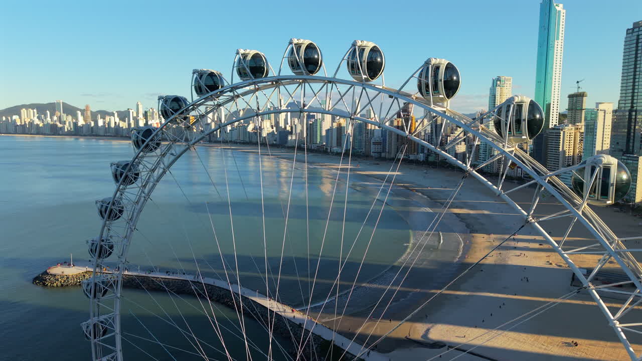 Smooth drone orbit clip around ferris wheel’s white structure, framing it against a waking city and endless ocean. Perfect for destination marketing reels