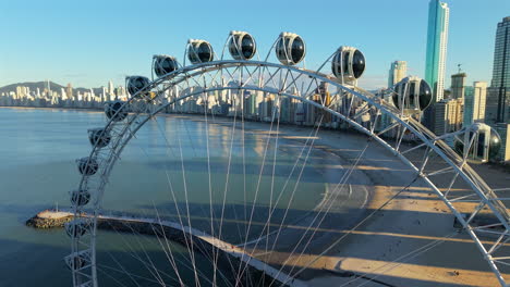 smooth drone orbit clip around ferris wheel’s white structure, framing it against a waking city and endless ocean. perfect for destination marketing reels