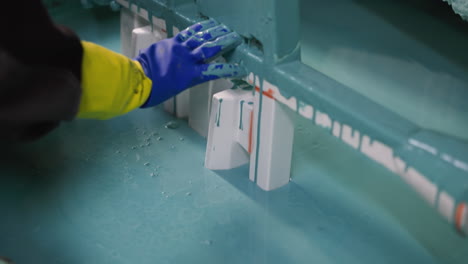 close-up of a gloved hand arranging white polymer products on a turquoise surface, detailing precision in manufacturing