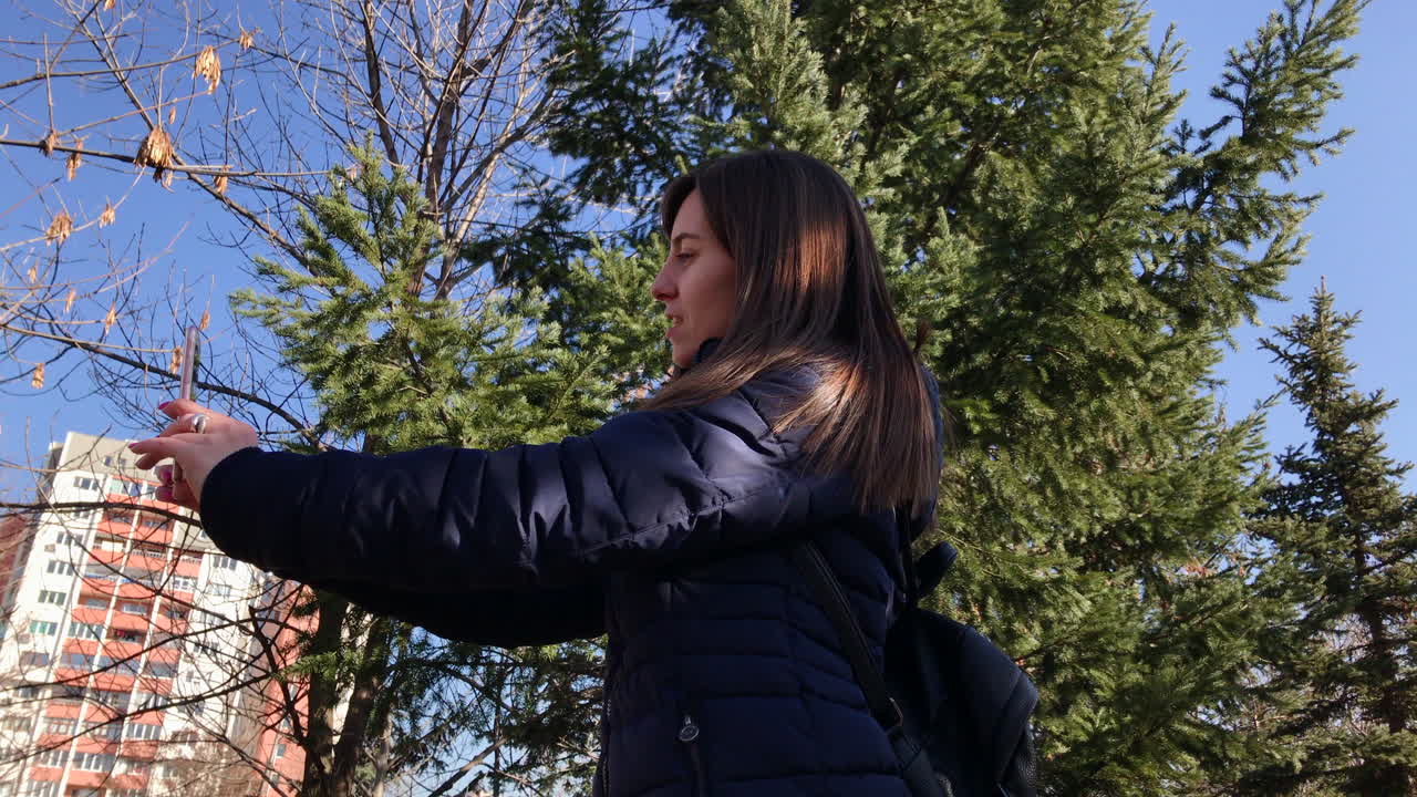 도시 공원에서 전면 카메라를 사용하여 스마트폰으로 셀카를 찍는 어린 소녀의 중간 왼쪽 사진