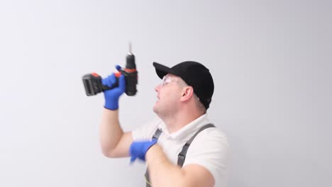 The Worker is Dancing Funny with an Electric Drill in His Hands on a White in the Studio. The worker is dancing funny with an electric drill in his hands on a white in the studio. The concept of home renovation. video