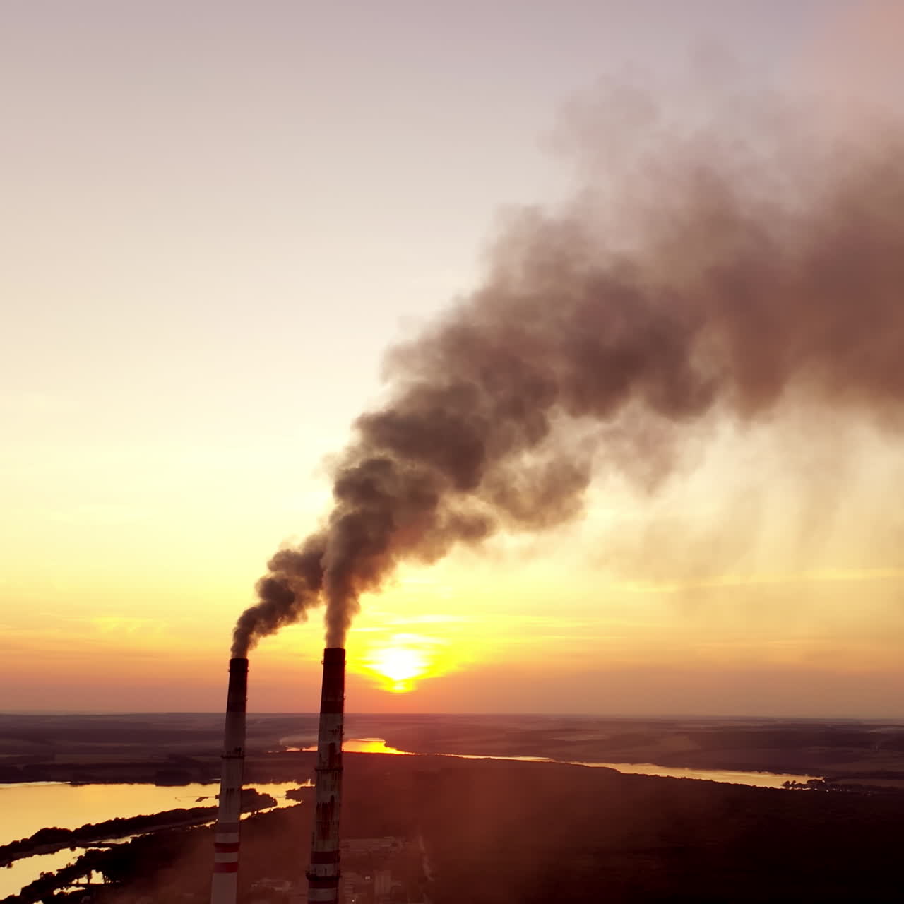 Pollution the atmosphere. Two factory pipes throw dirty emissions. Smoke looks beautiful but dangerous at sunset. Power plant on the beautiful landscape in the evening.