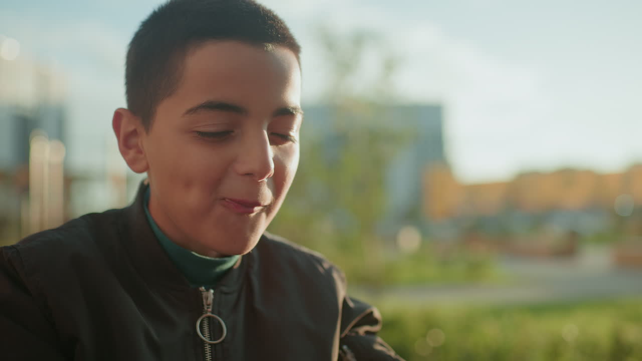 Close up of boy eating pizza outdoors, savoring taste with focused expression under warm daylight, casual atmosphere showing enjoyment of food during relaxed urban moment