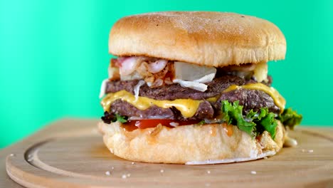 una hamburguesa grande con queso, salsa y verduras está girando rápidamente en una tabla de madera frente al fondo de la pantalla verde.