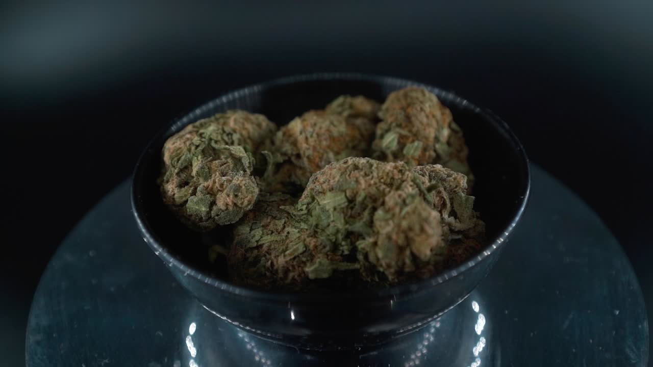 Dreamy Green Dried Marijuana Buds Close Up Shot, pile of dried marijuana plants in a shiny bowl, trichomes strains, on a reflecting rotating stand, studio lights, cinematic crane rotating slow motion