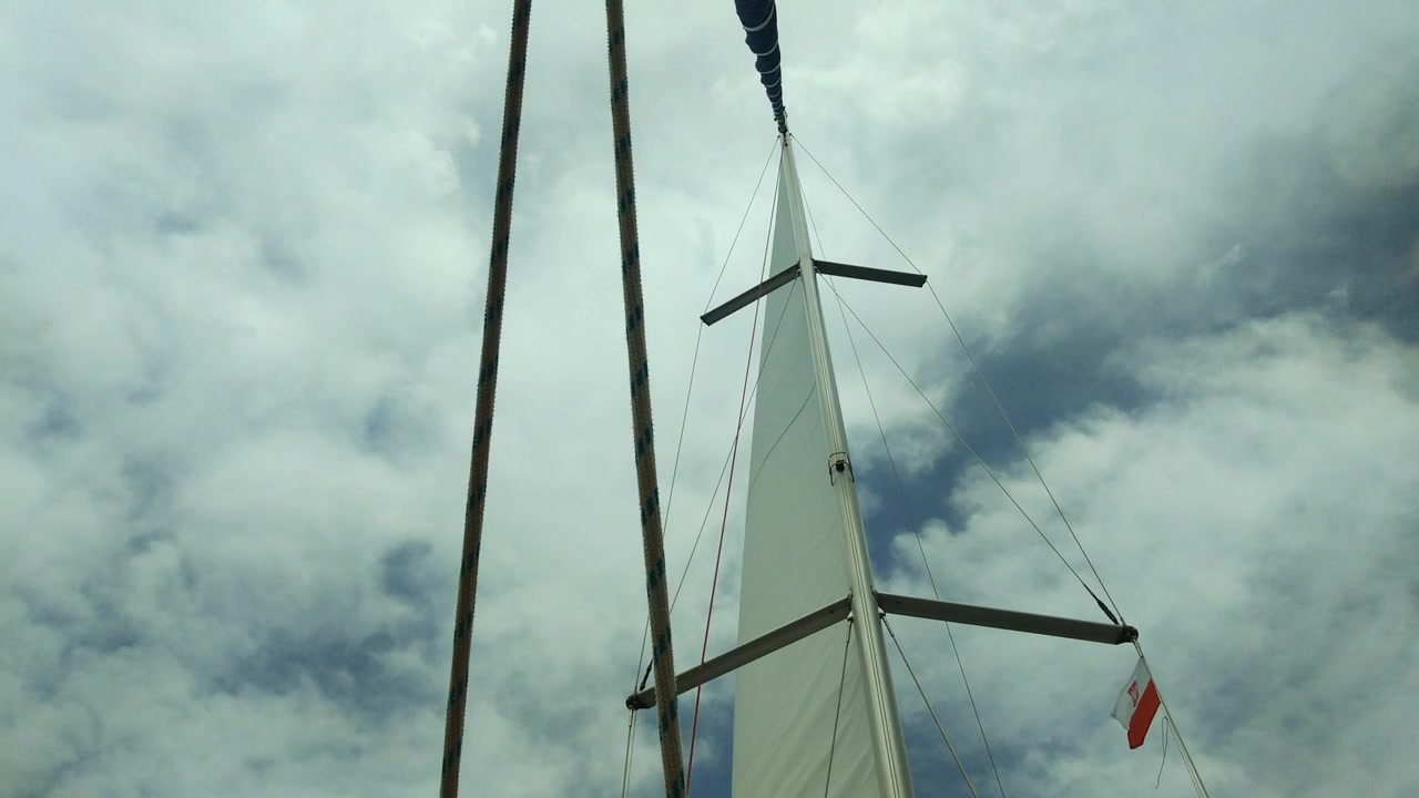 view of a sail on a mast with a polish flag on a windy and cloudy summer day