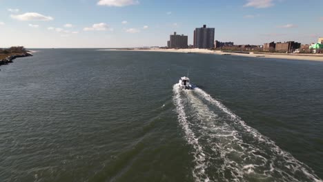 An-aerial-view-behind-a-fishing-boat-heading-out-to-sea-in-the-East-Rockaway-Inlet-in-Queens,-NY-on-a-sunny-day