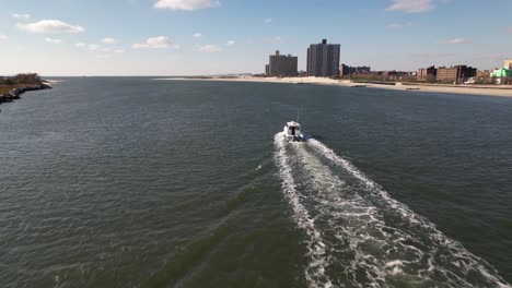 an aerial view behind a fishing boat heading out to sea in the east rockaway inlet in queens, ny on a sunny day