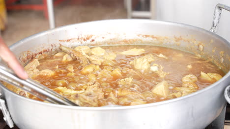 Stirring-the-pork-soup-with-a-large-spoon,-street-food-in-Ecuador