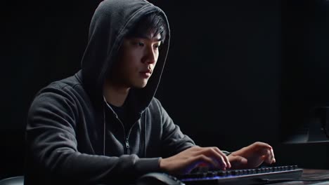 focused young man in hoodie engaging with keyboard in dimly lit environment, symbolizing concentration and digital interaction