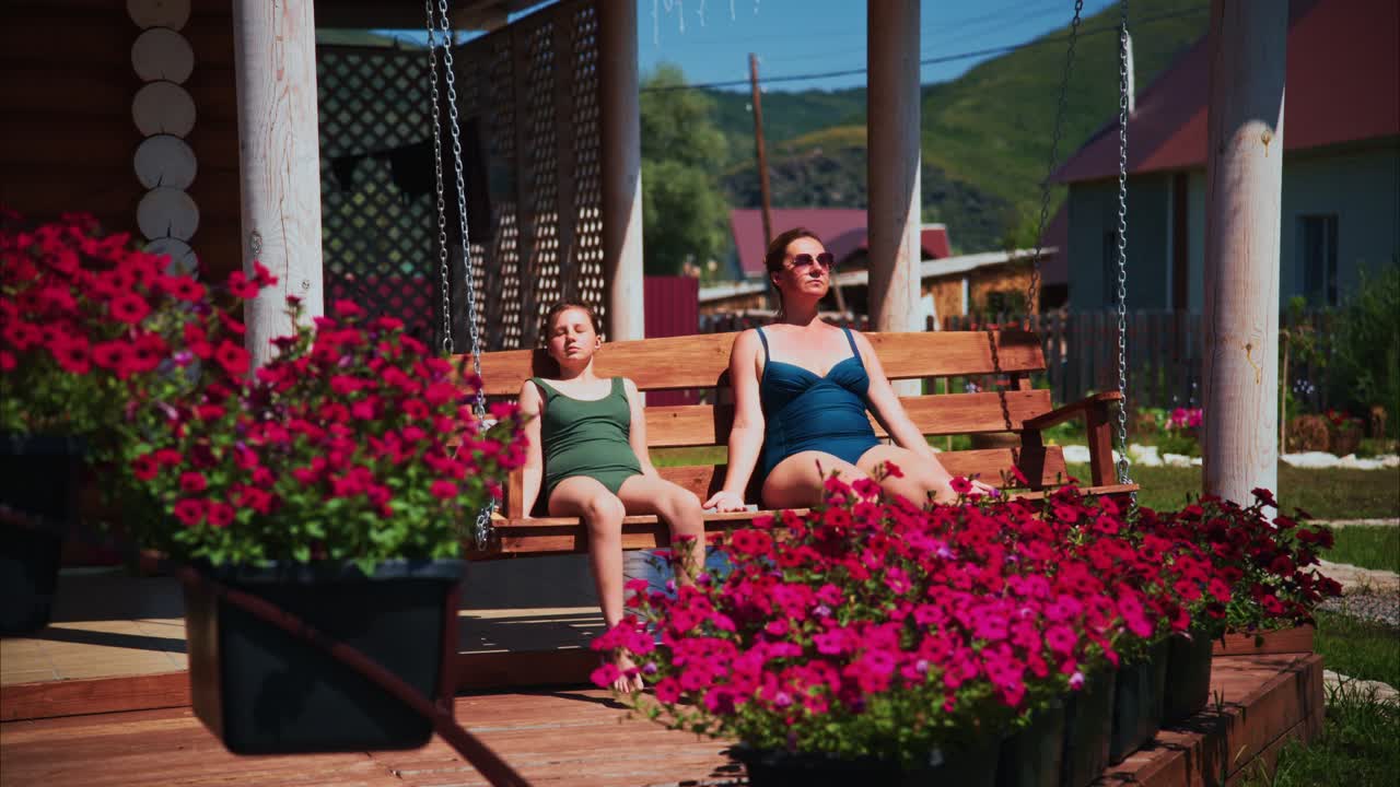 Donna e bambina che si rilassano su un'altalena da portico in una giornata di sole