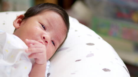 stretching its arms and twitching its face, a sleepy newborn baby is slightly closing its eyes as it is lying on a mattress inside a crib