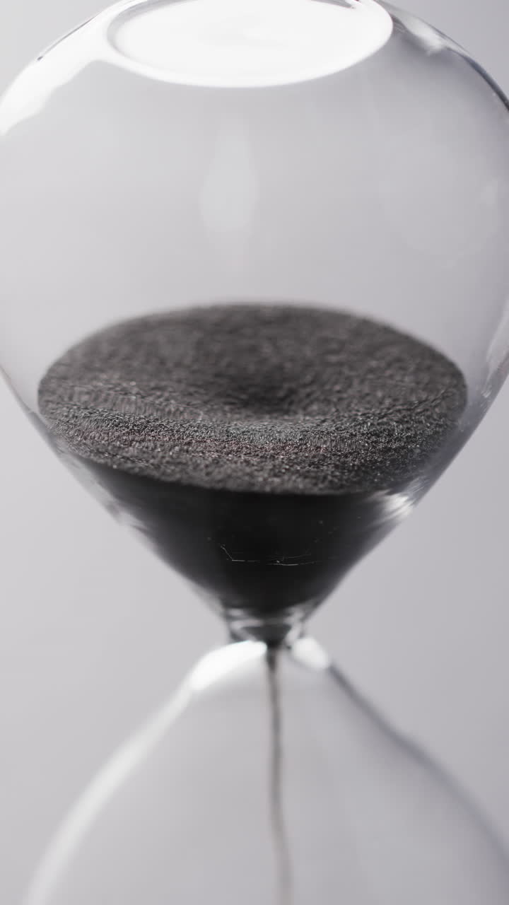 Vertical video of hourglass with sand pouring, copy space on white background