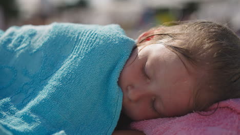 little girl covered with terry towel sleeps on deck chair