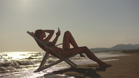 woman relaxing on a beach chair, taking a photo with her smartphone