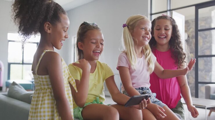 Vídeo de meninas diversas sentadas na sala comum da escola com um smartphone, conversando e rindo