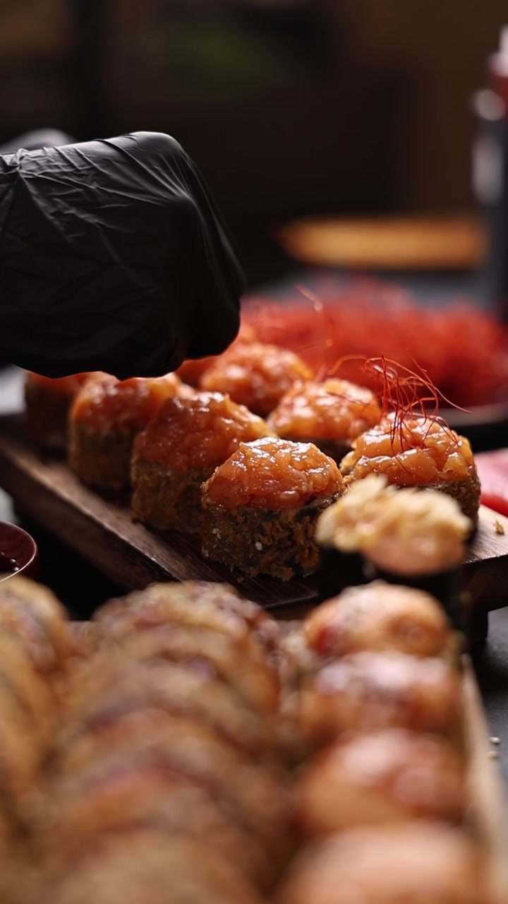Chef professionista che guarnisce sushi roll cotti al forno con fili di peperoncino.