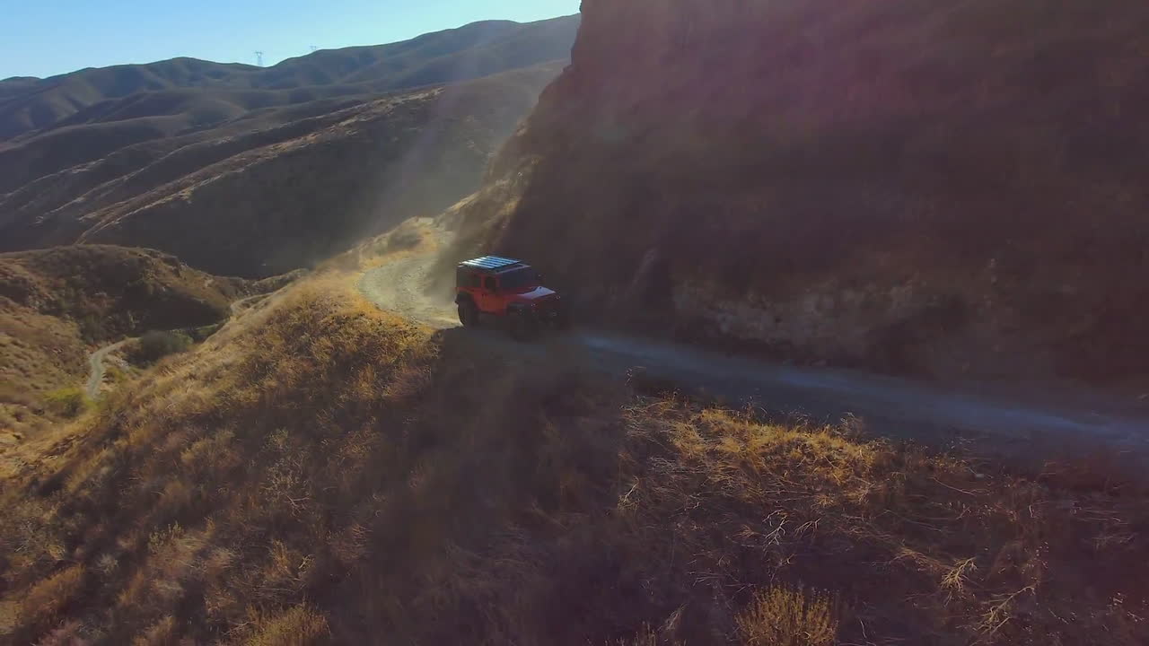 좁은 가파른 비포장 도로에서 오프로드를 운전하는 빨간색 지프, 공중 드론 보기