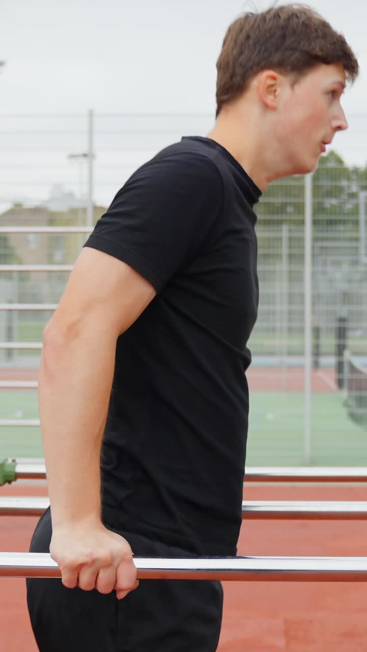 Close up of young caucasian man engaging in an outdoor calisthenics workout, performing dips on parallel bars, building upper body strength and muscle in an urban gym setting, vertical slow motion pan