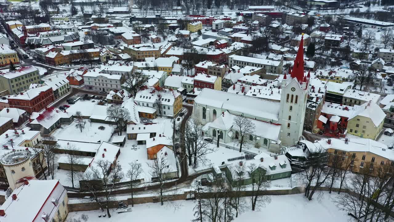 Ciudad de Cēsis en Letonia con edificios históricos e iglesia cubiertos de nieve blanca, vista aérea invernal con nevada